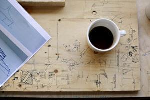 Puinen suunnittelupöytä kuvattu ylhäältä päin. Pöydällä myös suunnittelupaperi ja kahvikuppi.