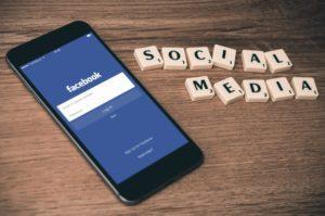 Sosiaalisen median koulutus, kuvituskuva. Kuvassa puhelin, jossa esillä Facebook ja pöydällä teksti ''social media''.
