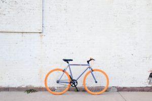 Oranssi-sininen polkupyörä valkoisen tiiliseinän edustalla.