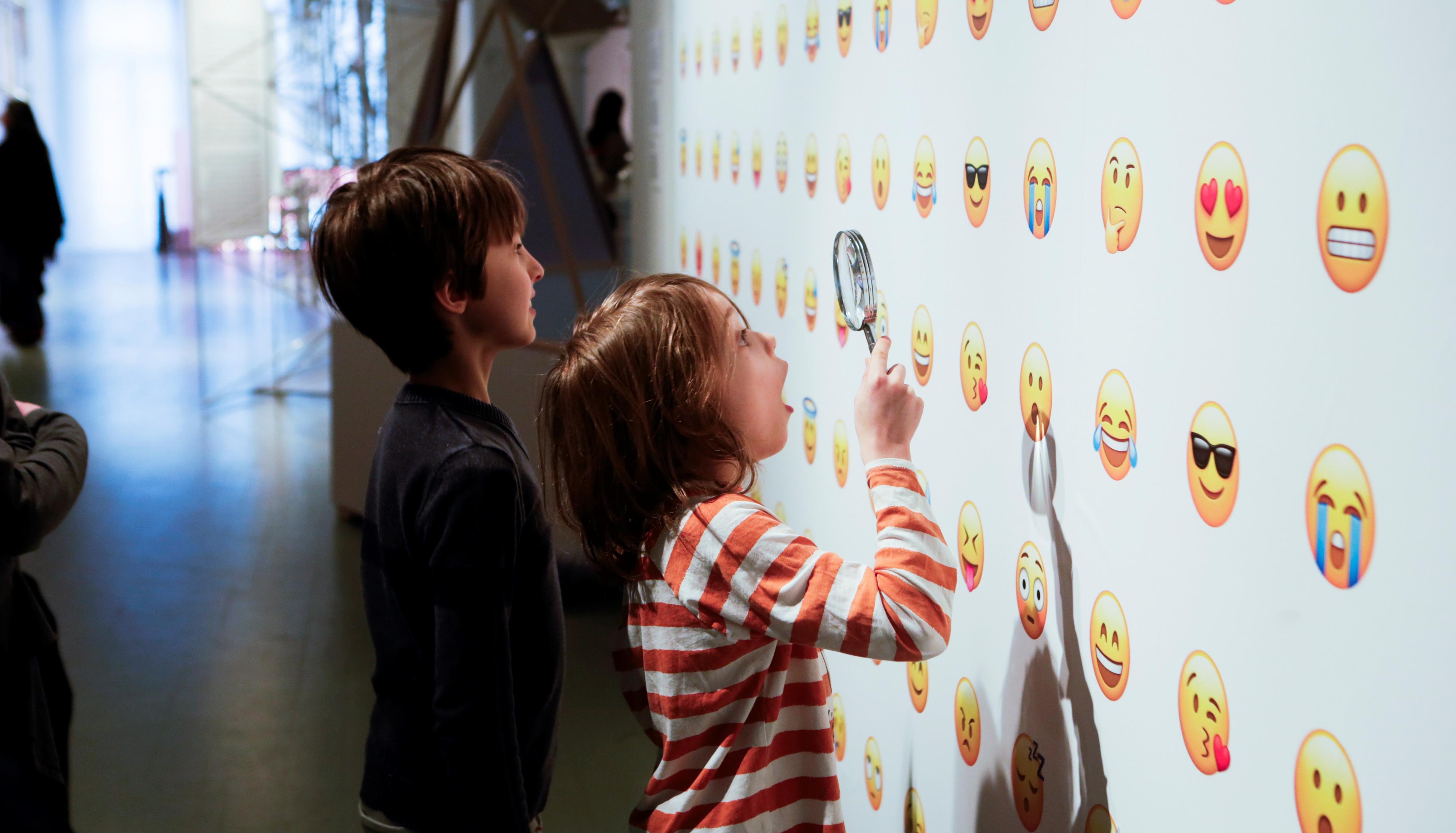 Lapset katselevat suurennuslasin läpi emojeilla koristeltua seinää