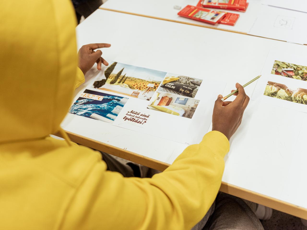Oppilas istumassa pöydän ääressä kuva kädessä ja katsomassa kollaasia, jossa keskellä teksti: Mitä sinä haluat tulevalta työltäsi?